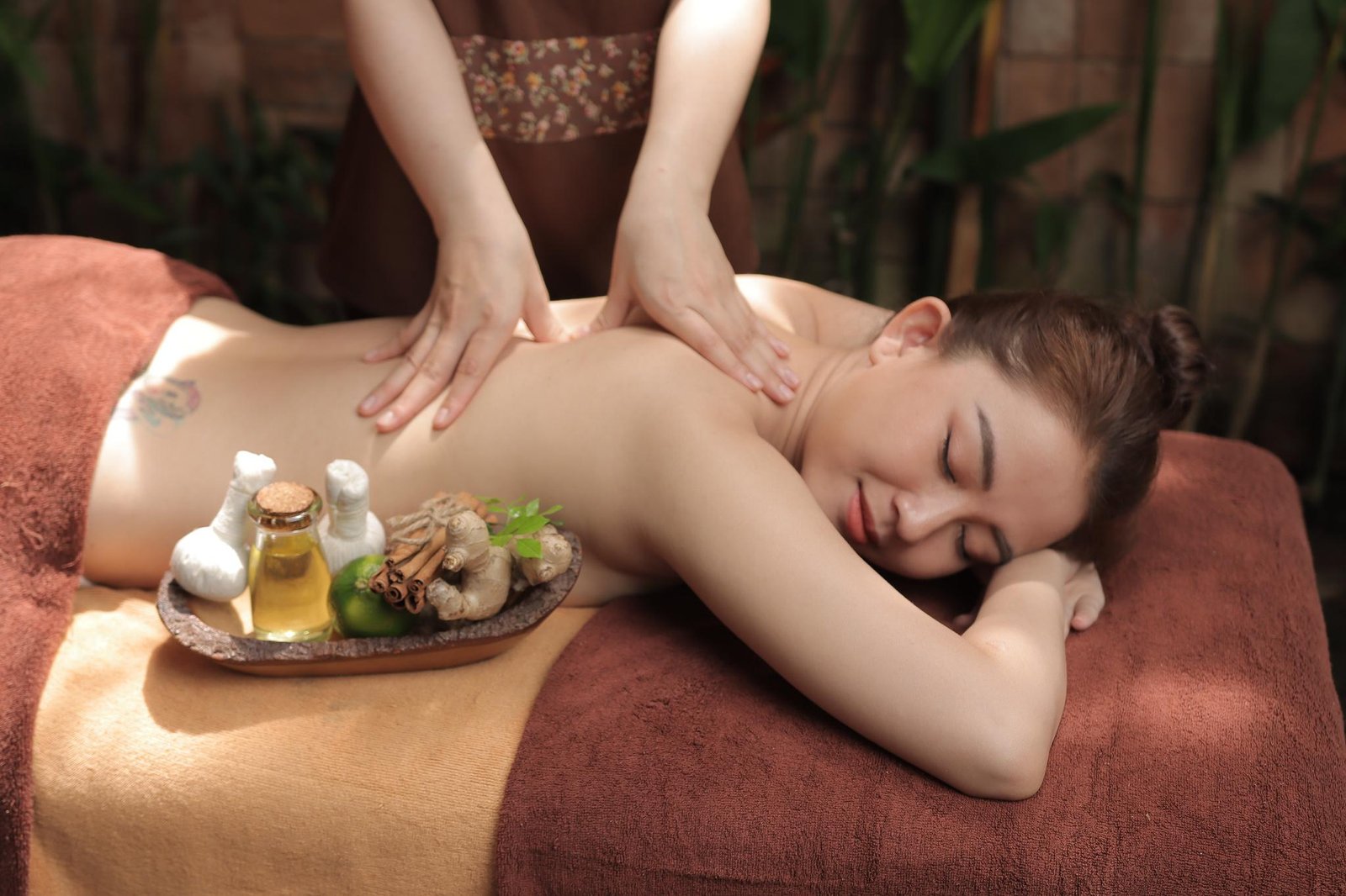 Người đang được massage lưng thư giãn với khay chứa các nguyên liệu tự nhiên như gừng, quế và dầu.