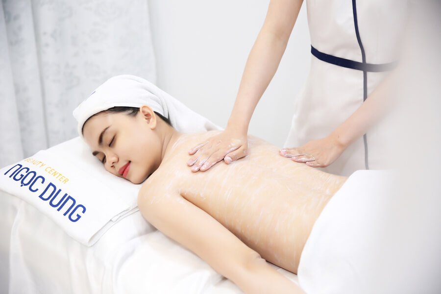 Người đang được massage thư giãn tại spa, nằm trên giường với khăn tắm trắng quấn quanh đầu.