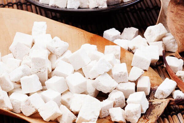 Các khối vuông màu trắng nhỏ được xếp trên bề mặt gỗ, có vẻ như là thực phẩm hoặc nguyên liệu chế biến.