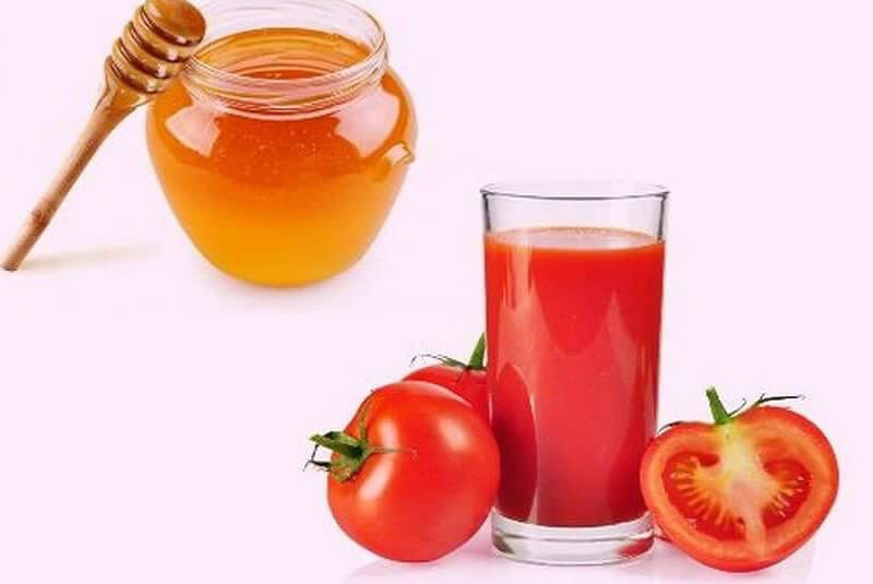 Hũ mật ong với thìa gỗ, ly nước ép cà chua và cà chua nguyên trái, cắt đôi trên nền trắng.