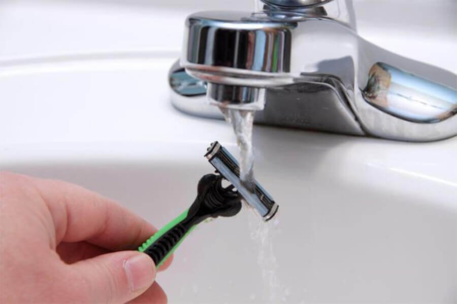 Người dùng đang rửa dao cạo dưới vòi nước chảy trong bồn rửa.