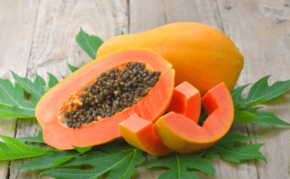 Quả đu đủ chín được cắt ra, lộ phần thịt màu cam và hạt đen, đặt trên lá xanh và nền gỗ.