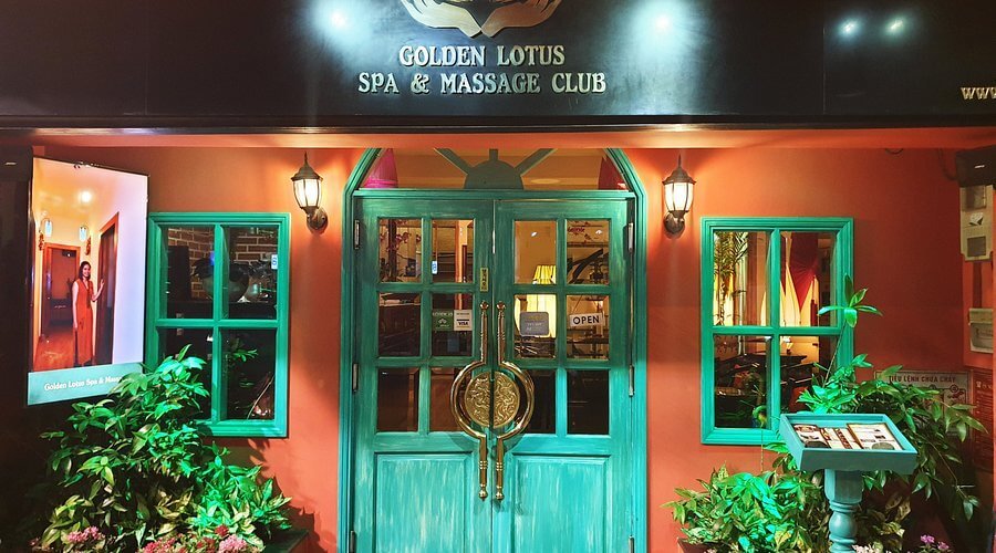 Mặt tiền của cơ sở spa với cửa gỗ màu xanh, biển hiệu và cây xanh trang trí hai bên lối vào.