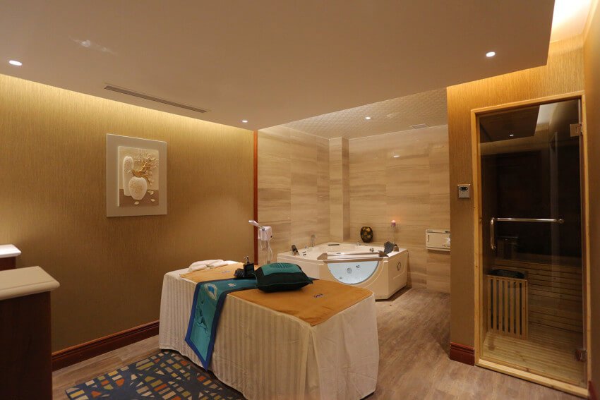 Phòng spa với giường massage, bồn tắm và phòng xông hơi, ánh sáng ấm áp tạo cảm giác thư giãn.