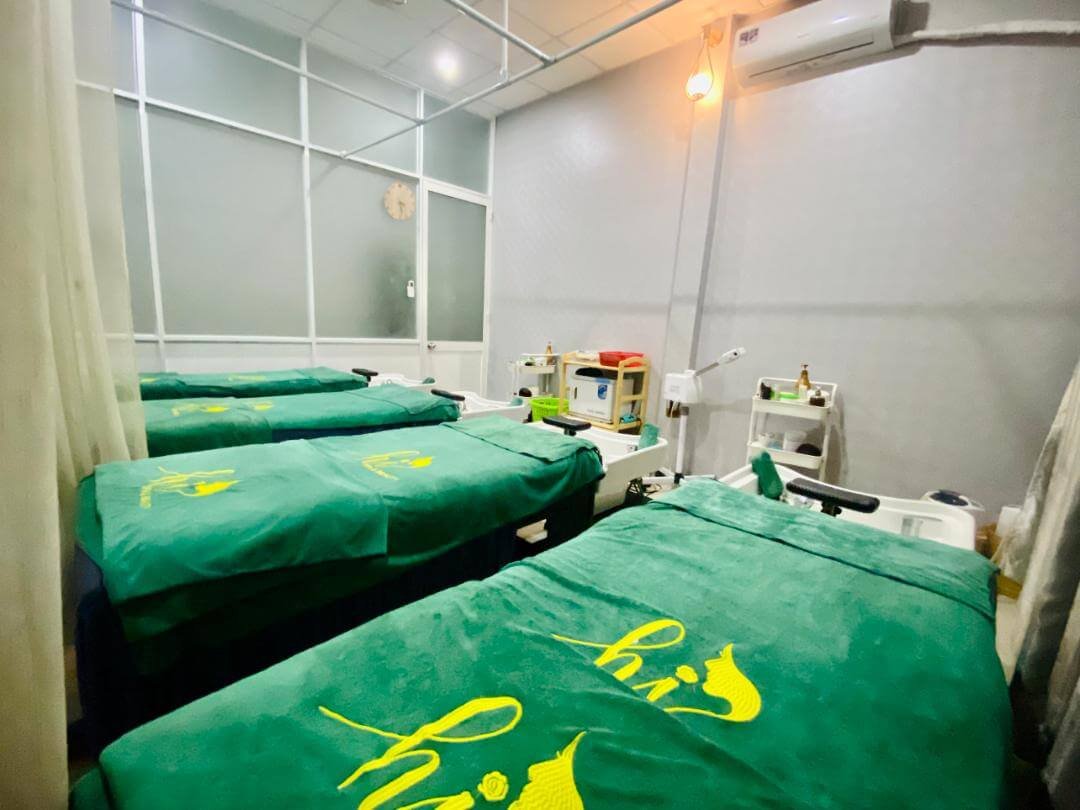 Ba giường massage phủ khăn xanh trong phòng spa, có rèm và thiết bị chăm sóc da.