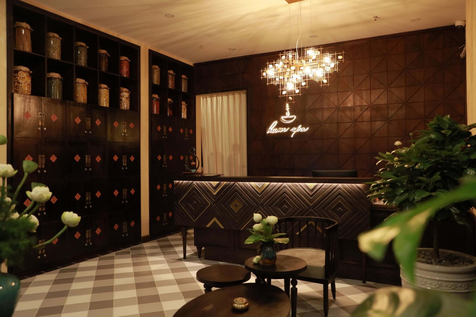 Quầy lễ tân spa với ánh sáng ấm cúng, bàn gỗ, kệ chứa lọ thủy tinh và cây xanh trang trí.