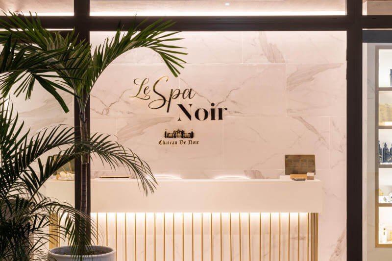 Khu vực lễ tân của spa với bảng hiệu "Le Spa Noir" trên tường đá cẩm thạch, trang trí cây xanh.