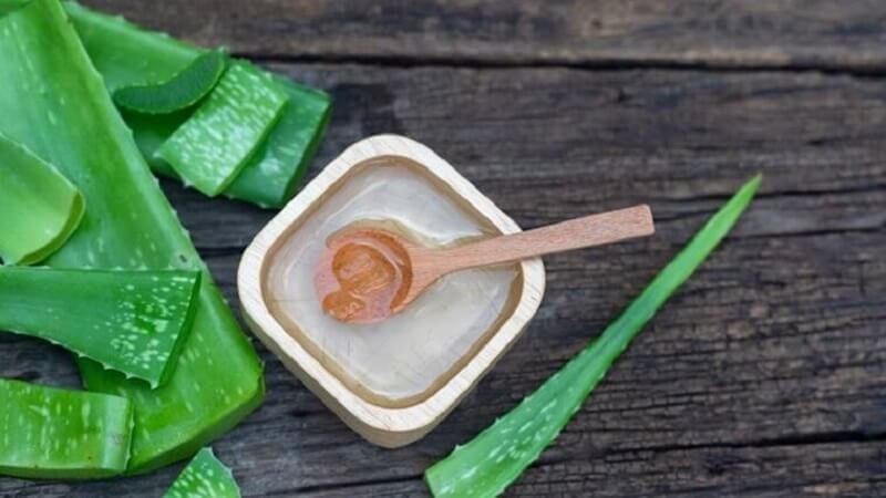 Lá nha đam tươi và một hũ nhỏ chứa gel nha đam cùng muỗng gỗ trên nền gỗ cũ.