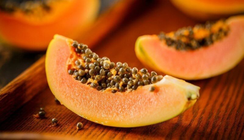 Miếng đu đủ chín cắt lát, màu cam, có hạt đen trên mặt, đặt trên bề mặt gỗ.