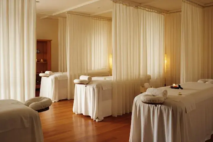 Phòng spa với giường massage, rèm trắng tạo không gian riêng tư, ánh sáng ấm áp từ đèn.