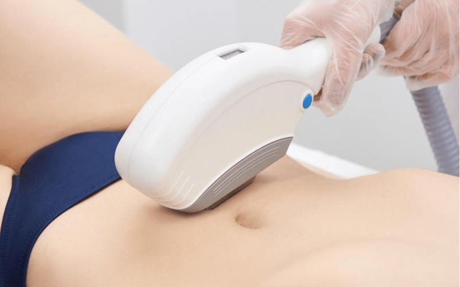 Người đang sử dụng thiết bị công nghệ làm đẹp trên vùng bụng, mặc đồ bơi màu xanh, tay đeo găng bảo vệ.