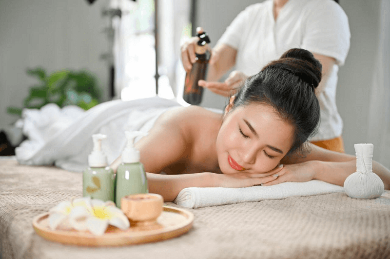 Người phụ nữ thư giãn trong spa với dầu massage, bên cạnh là các sản phẩm chăm sóc da.