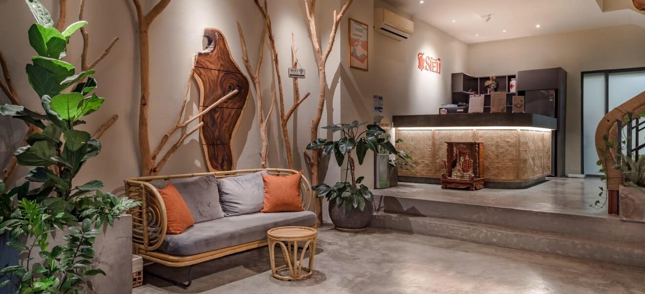 Khu vực lễ tân với ghế sofa, bàn gỗ và cây xanh, không gian ấm cúng và trang trí tự nhiên.