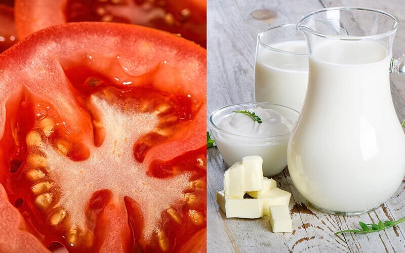 Cận cảnh lát cà chua đỏ bên trái, bên phải là sữa, bơ và kem trong ly và bình trên bàn gỗ.