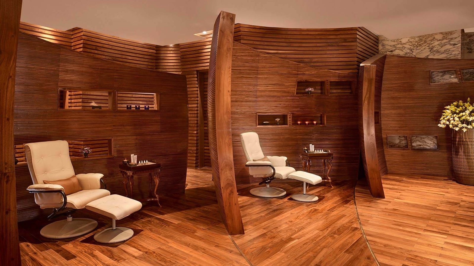 Phòng spa với ghế massage màu trắng, tường và sàn gỗ, trang trí bằng hoa và nến.