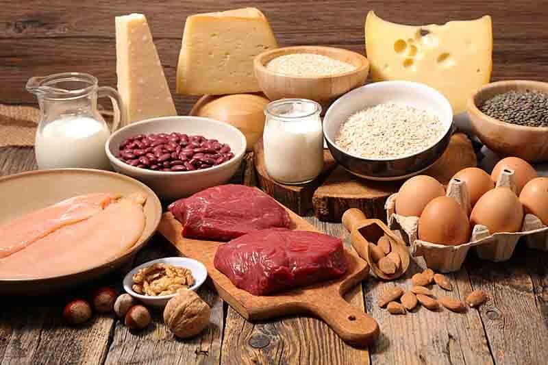 Đa dạng thực phẩm bao gồm thịt, trứng, sữa, các loại hạt và ngũ cốc trên bàn gỗ.