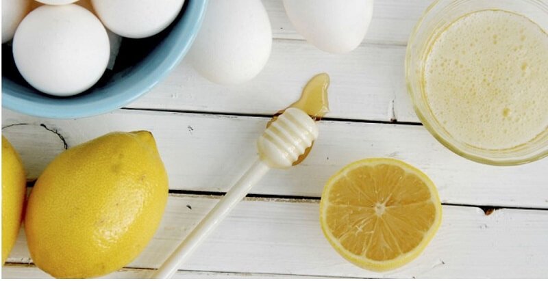 Làm Lông Nách Tự Rụng Có Được Không? Top 8 Cách Thực Hiện Đơn Giản 6 Quả chanh, trứng gà trong bát xanh, dụng cụ múc mật ong và ly nước chanh trên bàn gỗ trắng.