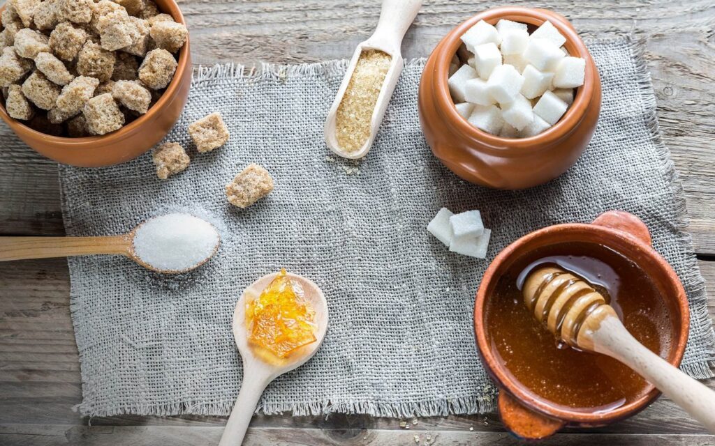 Các loại đường và mật ong trong bát, muỗng trên bàn gỗ, đặt trên khăn vải.