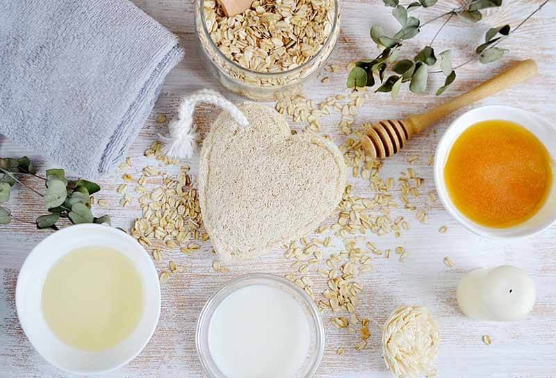 Bàn gỗ với bột yến mạch, mật ong, sữa, khăn xám và đồ trang trí cây xanh, tạo cảm giác thư giãn.
