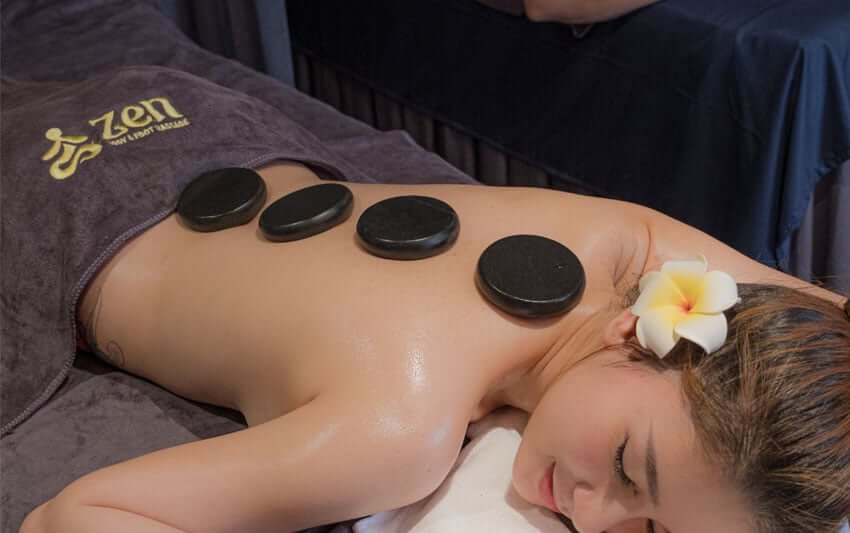 Người đang nằm thư giãn với bốn viên đá nóng đặt trên lưng, hoa cài trên tóc, trong phòng spa.